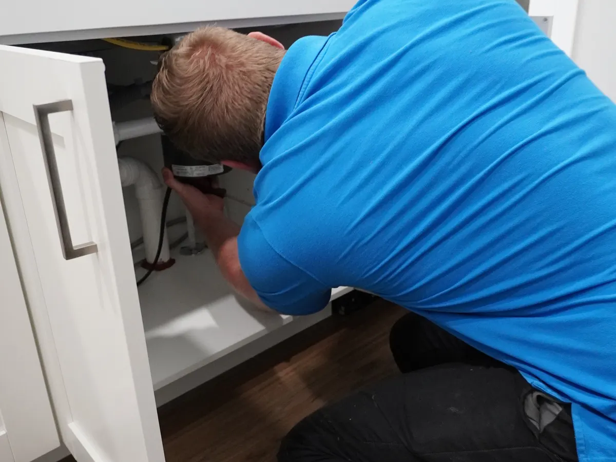 Technician accessing a garbage disposal under a kitchen sink during a repair visit