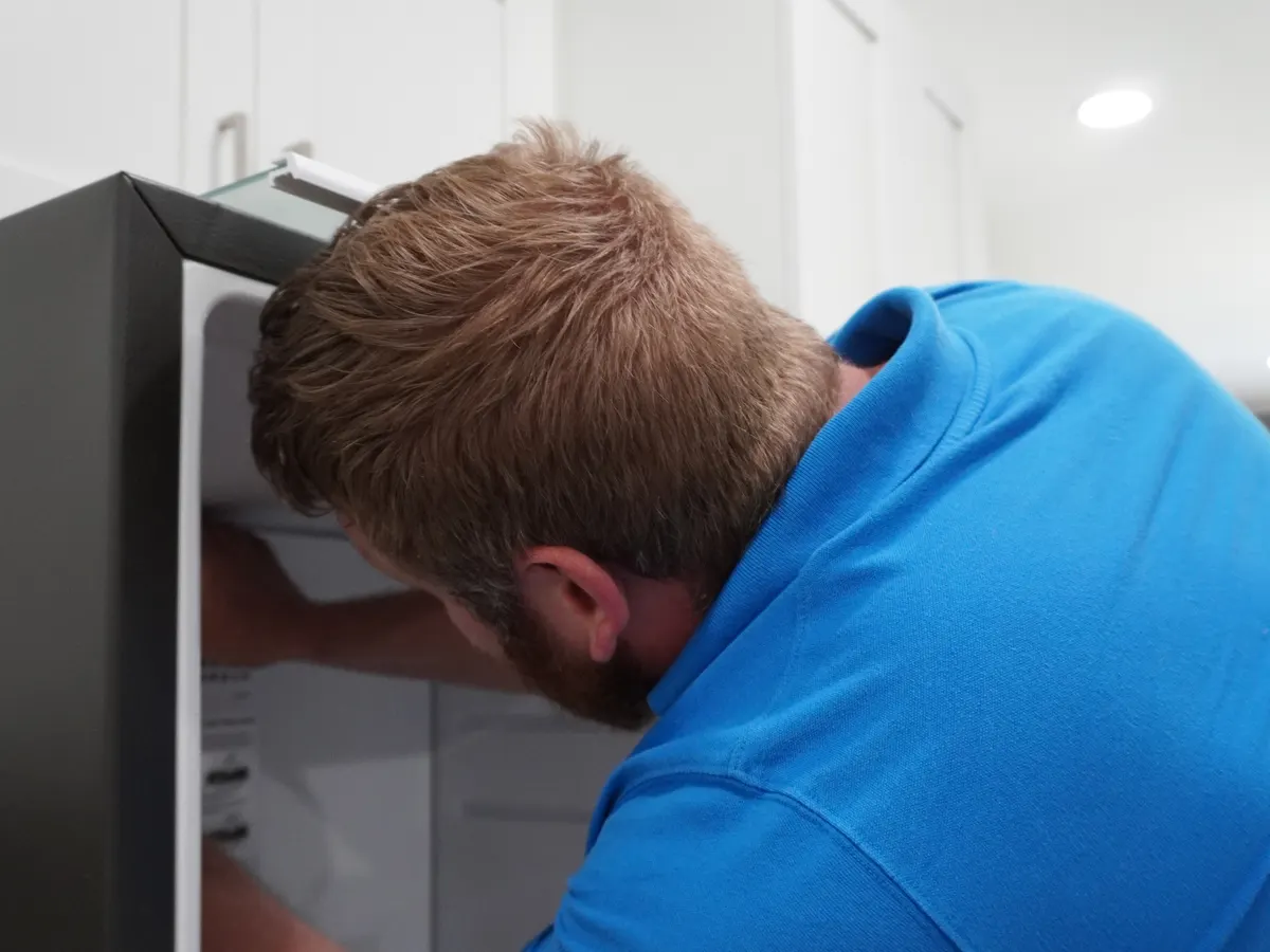Technician inspecting a refrigerator's freezer compartment during a repair visit