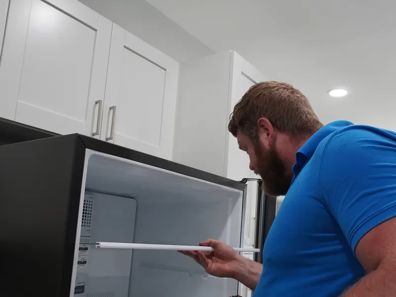 Nate Baird reinstalling a refrigerator shelf to finish up a repair visit