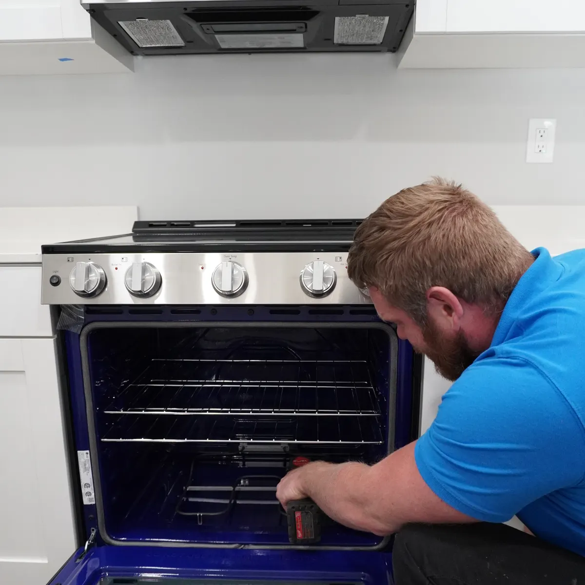 Technician testing a range's control panel with a screwdriver during a repair visit