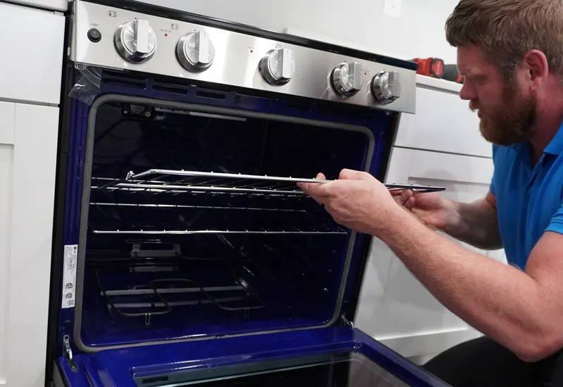 Technician inspecting the interior rack and door hinge of an open oven during a repair visit