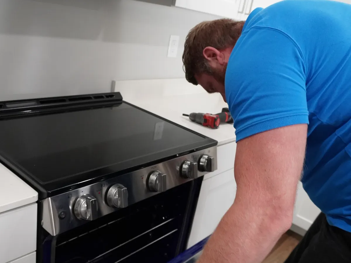 Technician testing a range's control panel and burner knobs with a multimeter