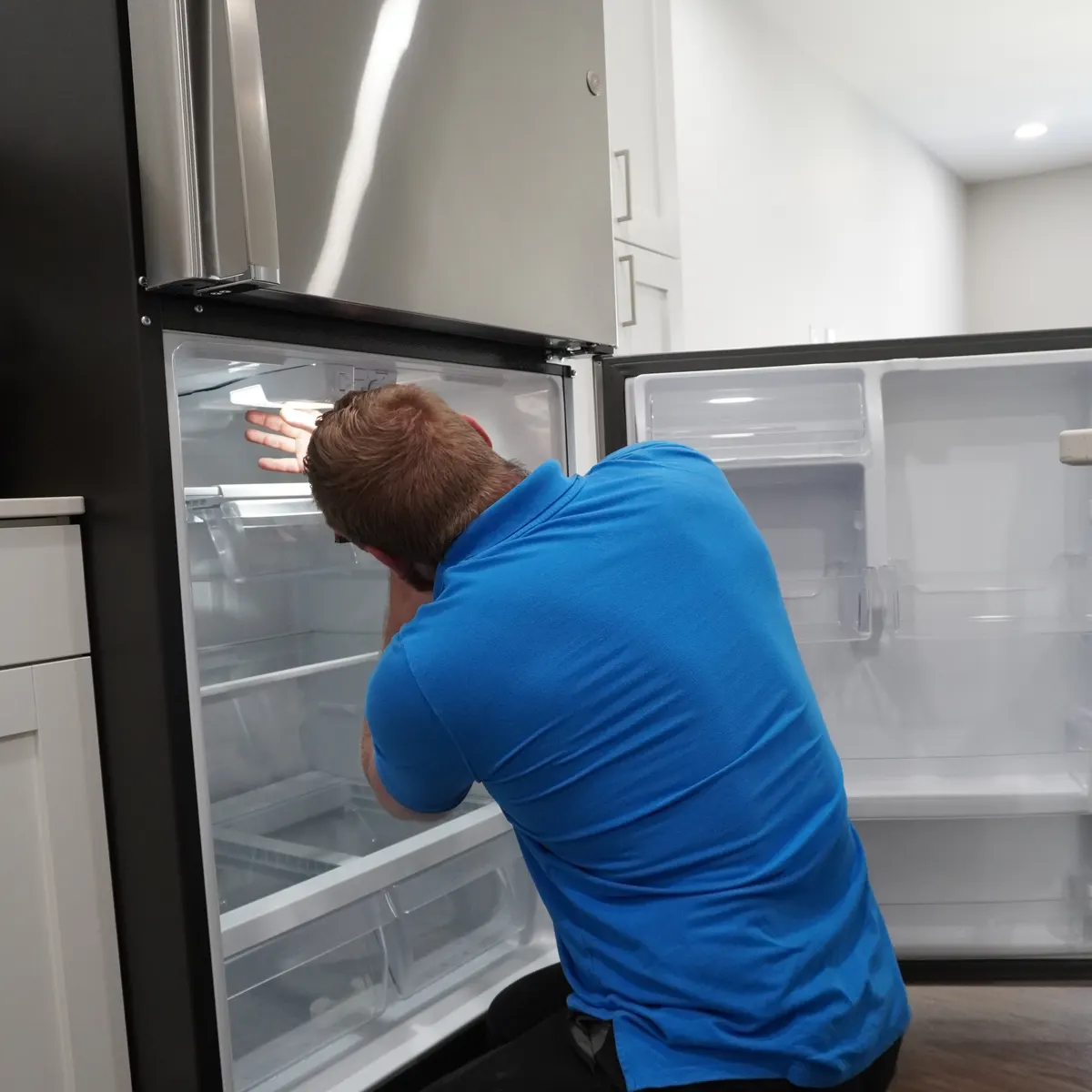 Technician inspecting the freezer side of a French-door refrigerator with both doors open